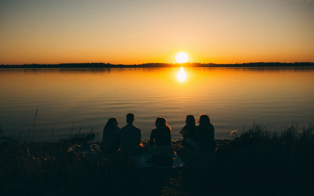 Porukka istumassa järven rannalla auringon laskussa