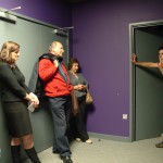a man, leaning on a half opened door, delivers a monologue to an audience of four in a small room painted purple