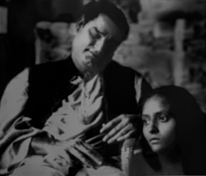 A man in a vest leans with closed eyes as a woman beside him looks on with a worried expression in a grayscale scene.