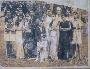 Old sepia-toned group photo of a large family standing and children seated in front, outdoors.