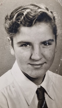 Black-and-white portrait of a young man with wavy hair wearing a white shirt and dark tie.