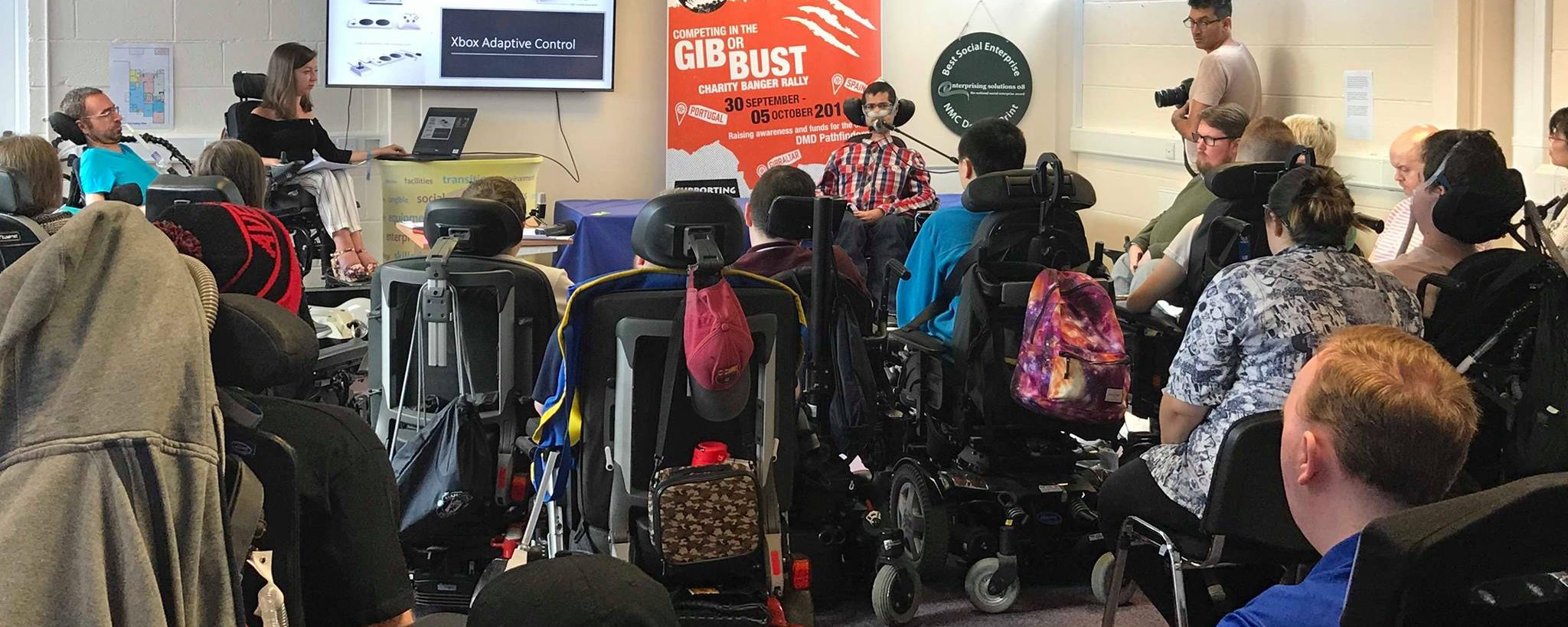 A group of young people in powerchairs attending a Pathfinders conference. The words "Xbox Adaptive Control" are visible on a screen.