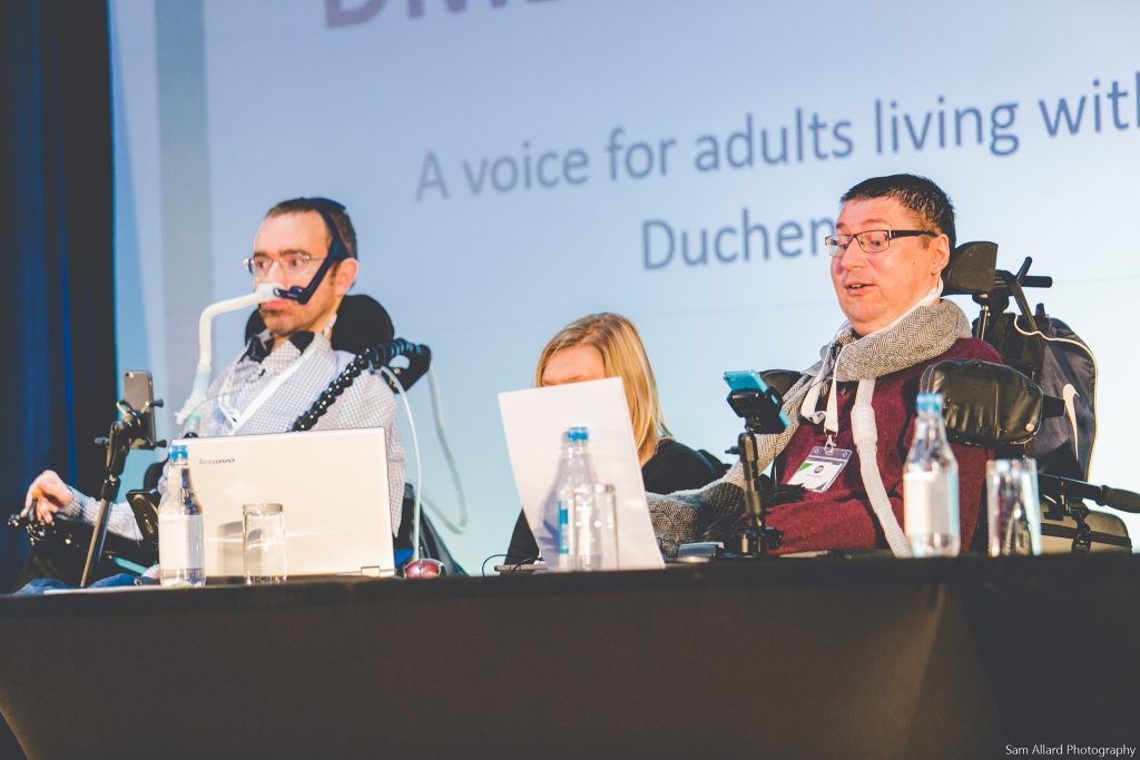 Jon Hastie and Mark Chapman sitting at a desk giving a presentation at the Action Duchenne International Conference