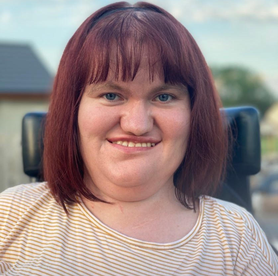 A photo of Michaela, a white woman with dark red hair, smiling at the camera.