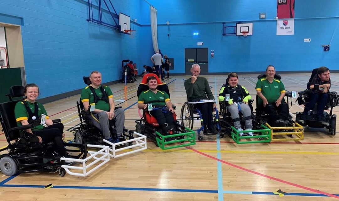 A group of powerchair football players lined up in a sports hall.