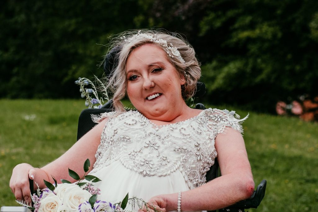 Suzanne with blonde hair in a black wheelchair wearing a wedding dress