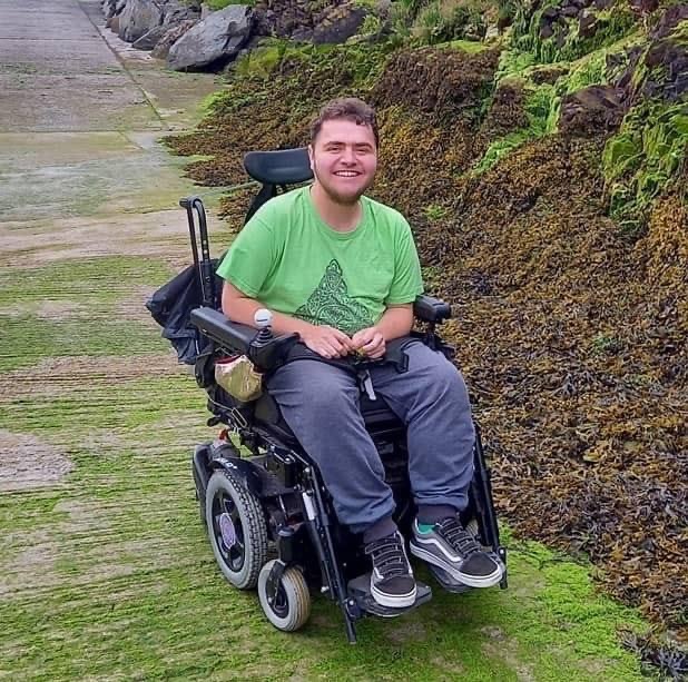 A picture of Sam Cornelius-Light, a white male smiling at the camera wearing a green t-shirt.