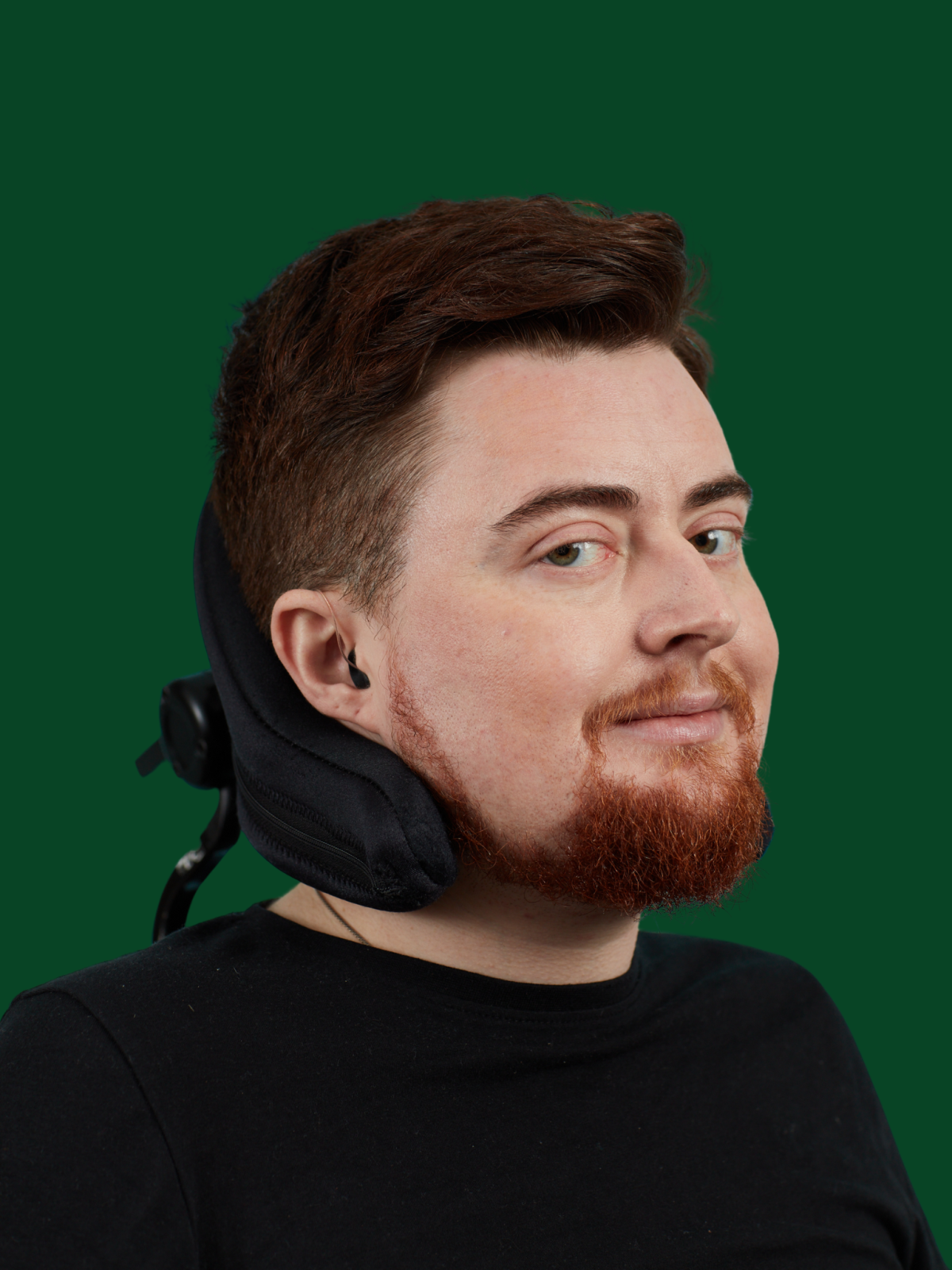 Head and shoulders image of Jamie Hale, a white person with dark red hair and a red beard, wearing black, with their head on a black wheelchair headrest
