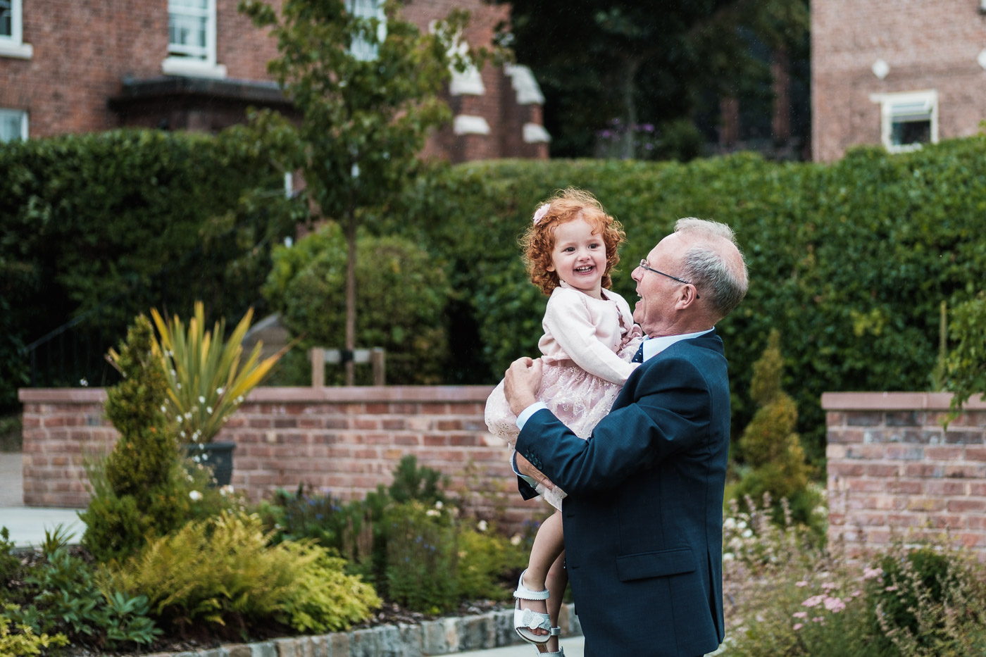 grandad has fun with his granddaughter in the grounds of the old palace in chester at his sons wedding