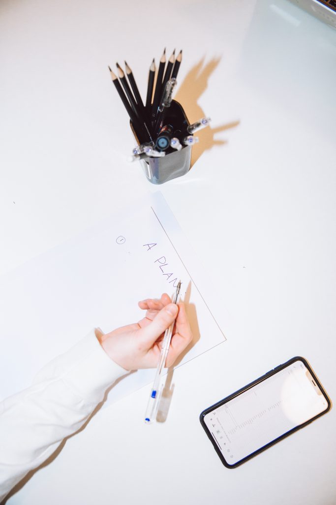 Foto van een witte bureau met blad waarop iemand een planning schrijft.