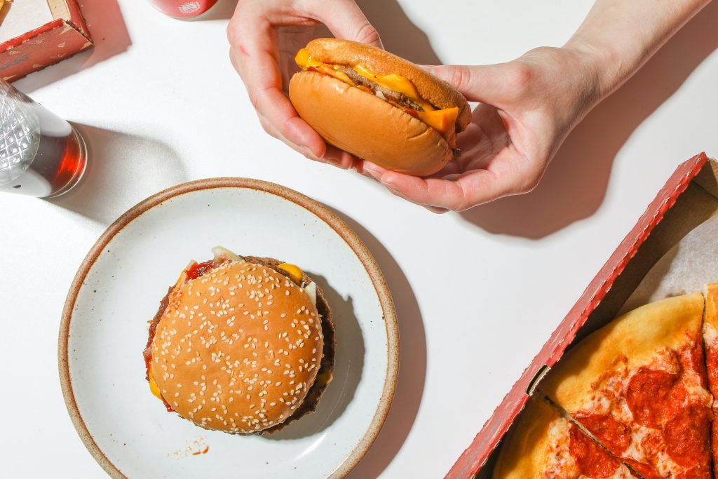 Foto van een tafel met 2 cheeseburgers en een stuk pizza.