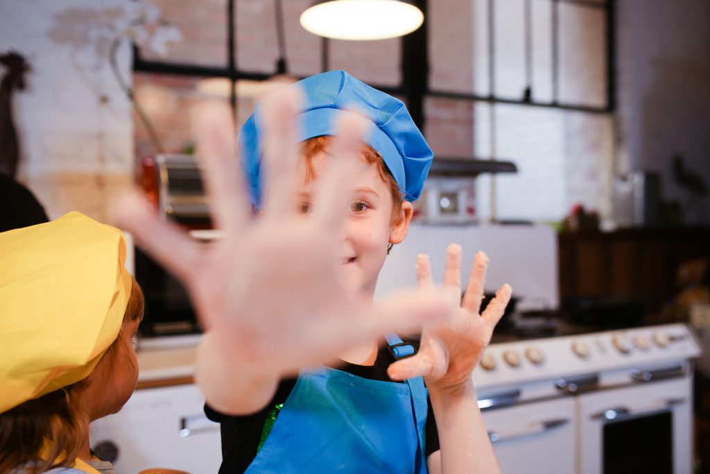 Foto van een jongen met koksmuts die zijn vuile handen toont.