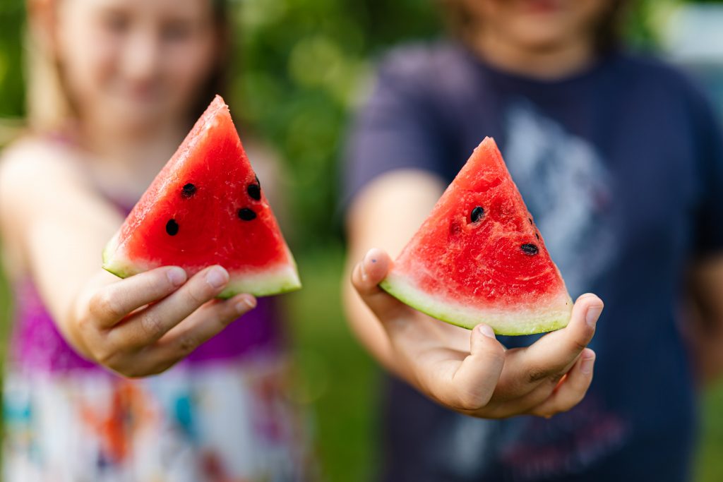 Foto van twee kinderen die een stukje watermeloen tonen aan de camera.