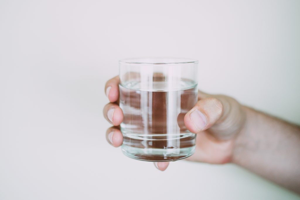 Foto van een hand dat een glas water vasthoudt.