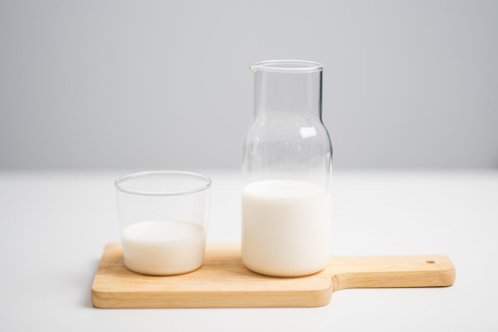 Foto van een kannetje melk met een glas ernaast.