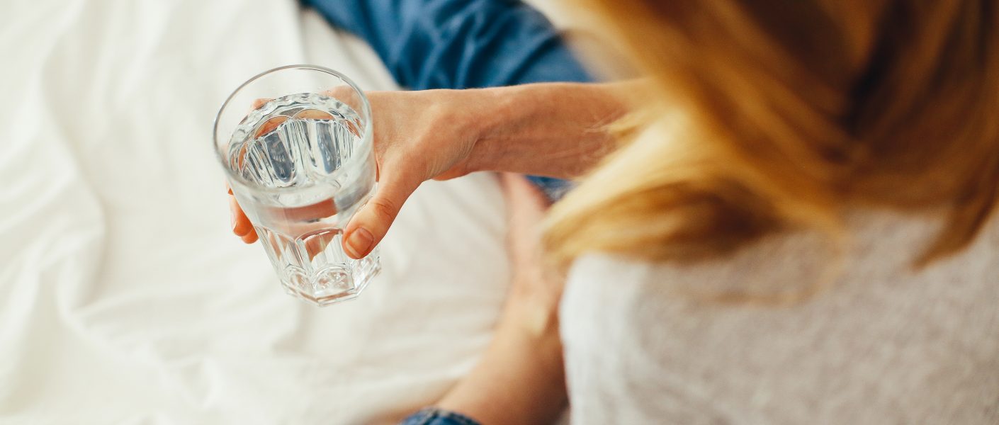 Foto van een vrouw met een glas water in de hand.