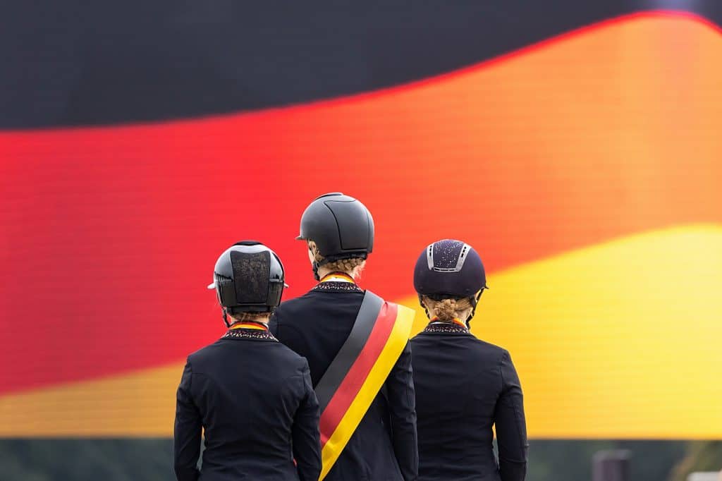 Siegerehrung DJM für die Junioren-Dressurreiterinnen vor der großen Deutschlandfahne auf dem Monitor. (Foto: J. Fellner)
