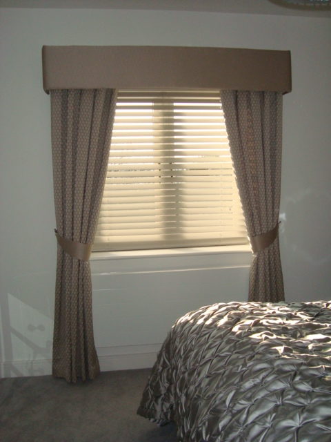 A bedroom window decorated with a pelmet, curtains with tiebacks and a set of Venetian
