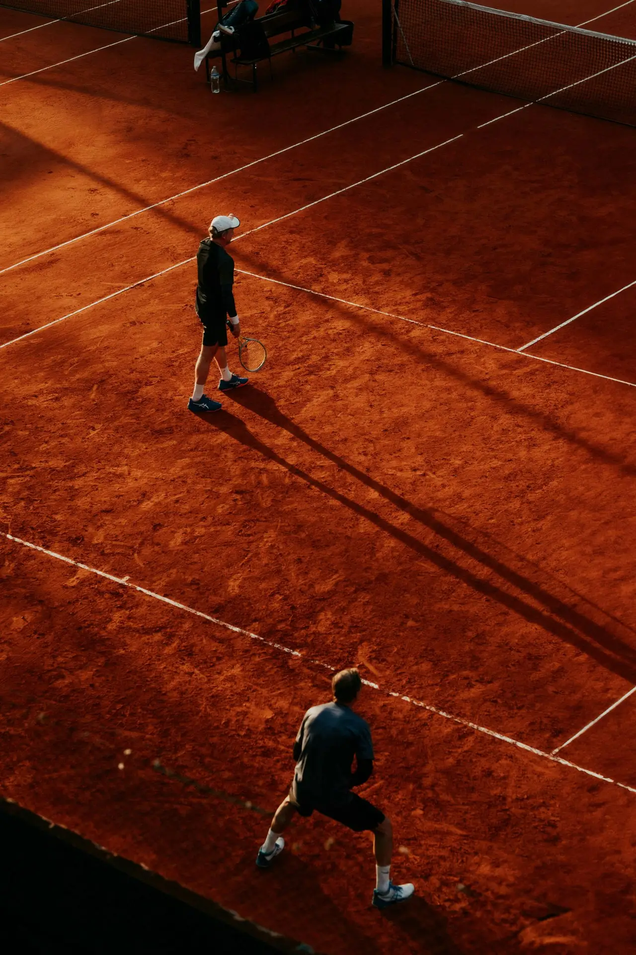 Shot of two tennis players on a clay court during sunset from an elevated angle.