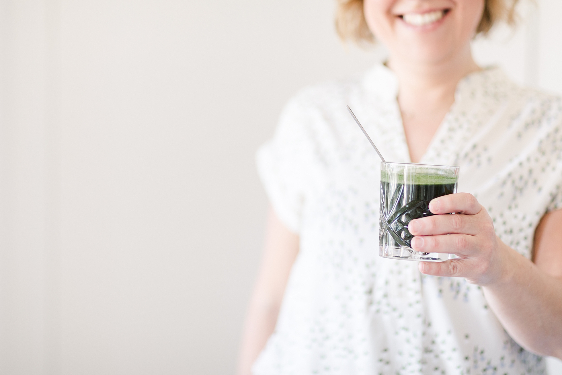 A smiling woman holding a green drink