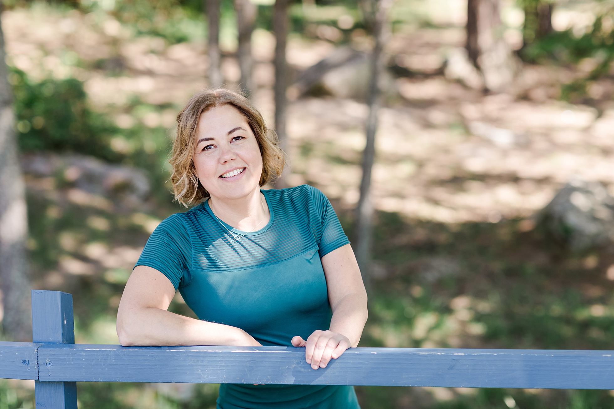 A woman dressed in a green yoga top leaning against a blue fence