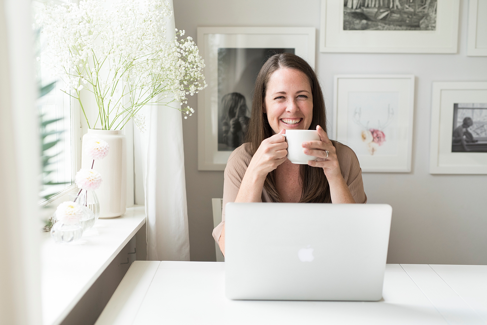 Photographer Janine Laag smiling and holding a cup of coffee while working at her computer