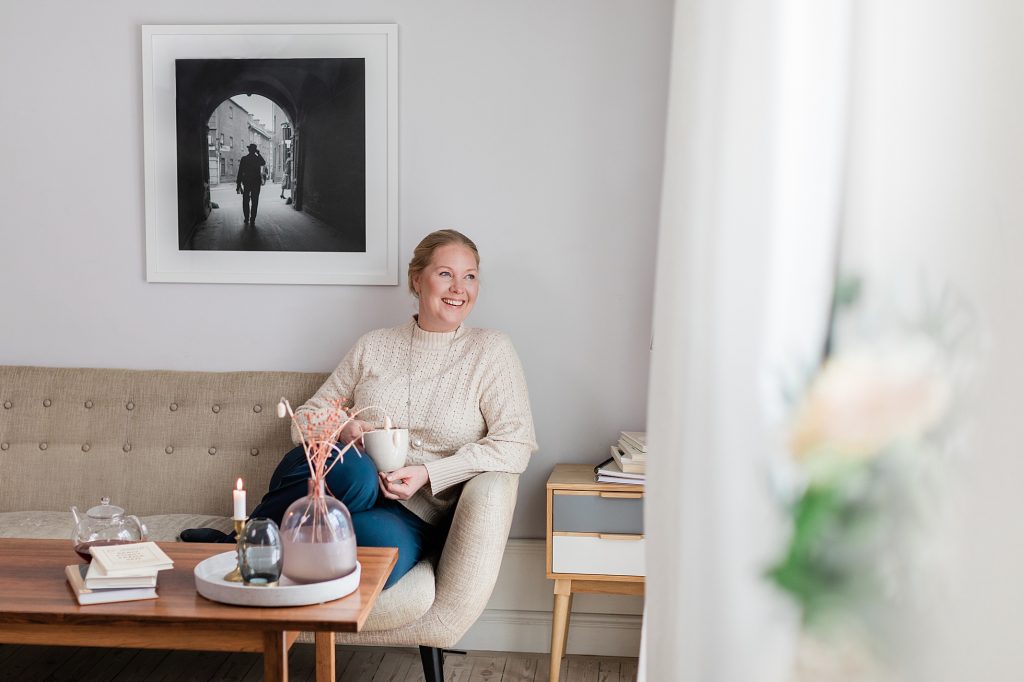 "a photo of a smiling business woman sitting in a pretty home holding a cup of tea taken by Janine Laag"
