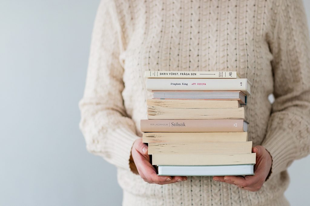"a close-up photo of a woman holding a pile of books"