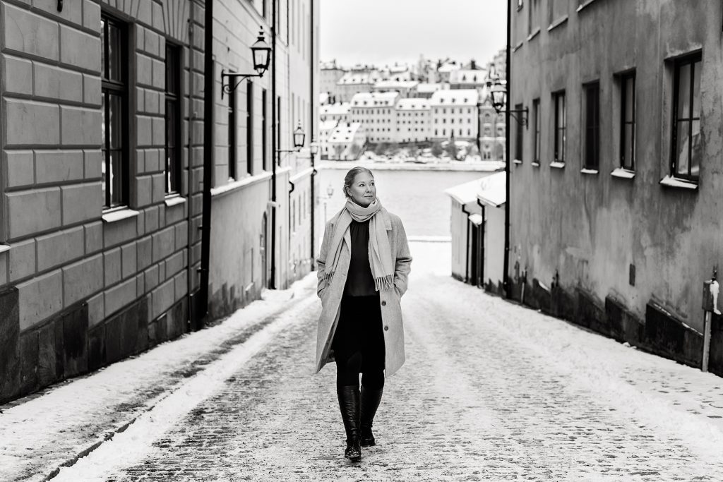 "a black and white photo of a stylish woman walking on Riddarholmen in Stockholm taken by Janine Laag at Lumeah Photography"