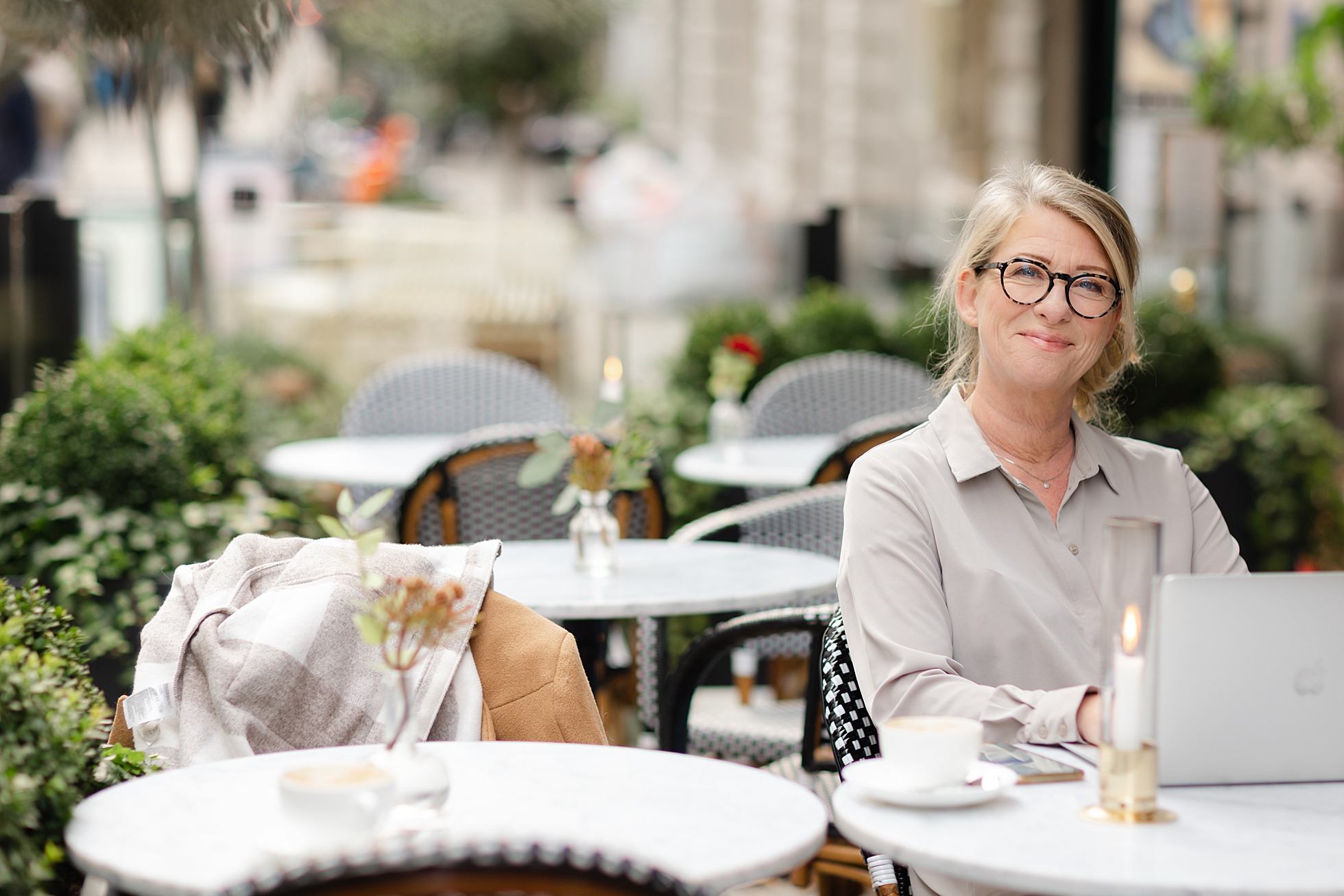 A photo of book publisher, Anette Nyberg, dressed in a grey top at an outdoor cafe in Stockholm while she works on her laptop