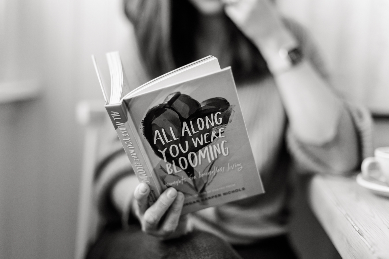 a black and white photo of a woman reading a booked called 'Alla long you were blooming'