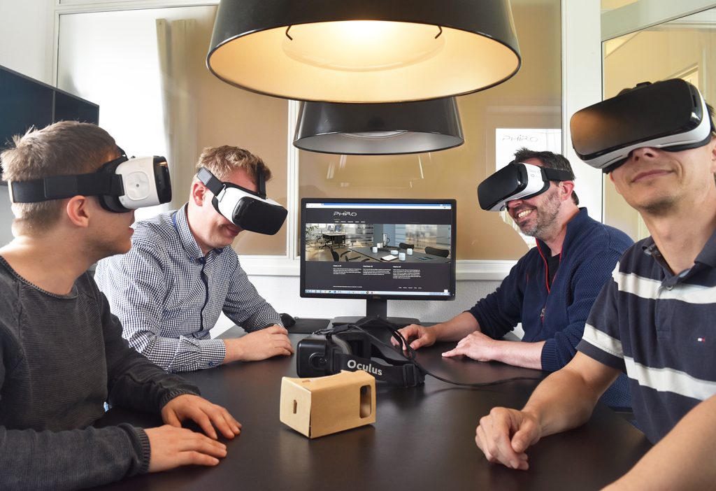 Fire mænd iført VR-briller rundt om et bord med en computerskærm.