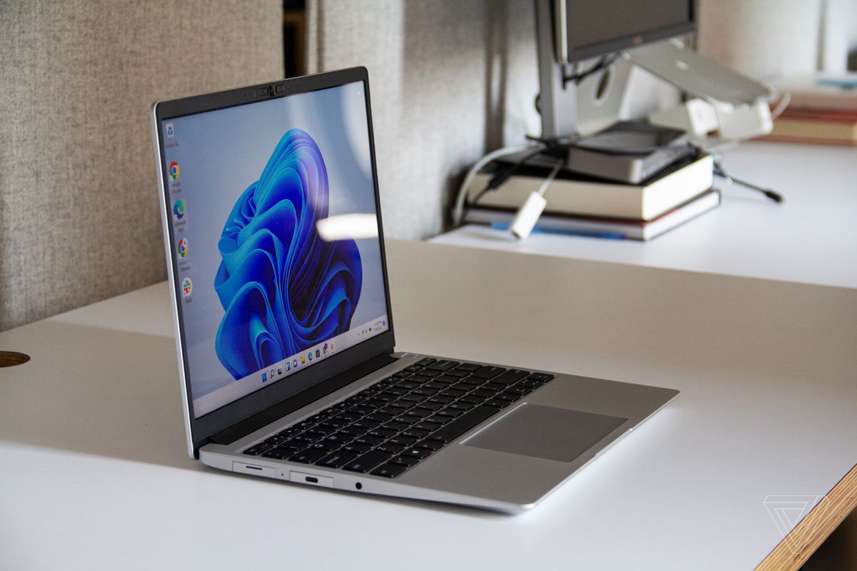 The Framework Laptop angled to the right on a desk seen from the left side. The screen displays a light blue desktop background with a dark blue flower.