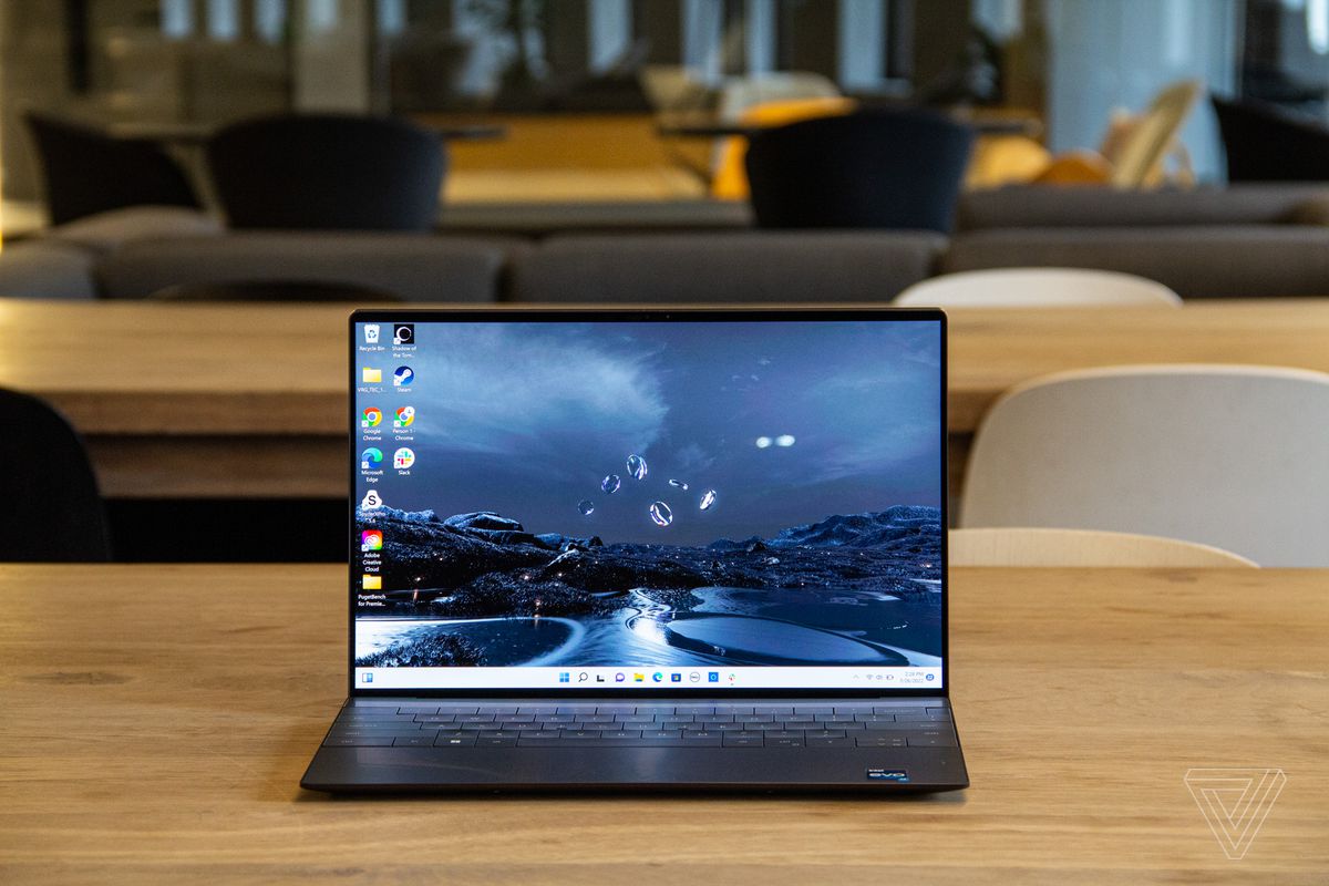The Dell XPS 13 Plus open on a wooden table seen from the front. The screen displays a river at night as a Windows desktop background.