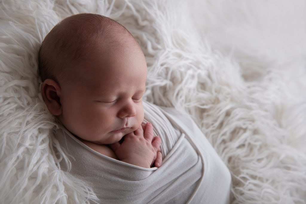 Sovande bebis på vit fäll, fotograferad i motljus