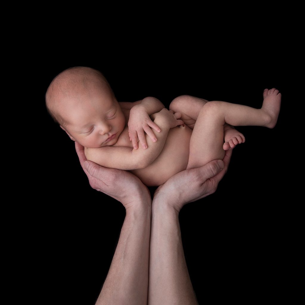 Nyfödd bebis fotograferad i studio, liggandes på mörk bakgrund