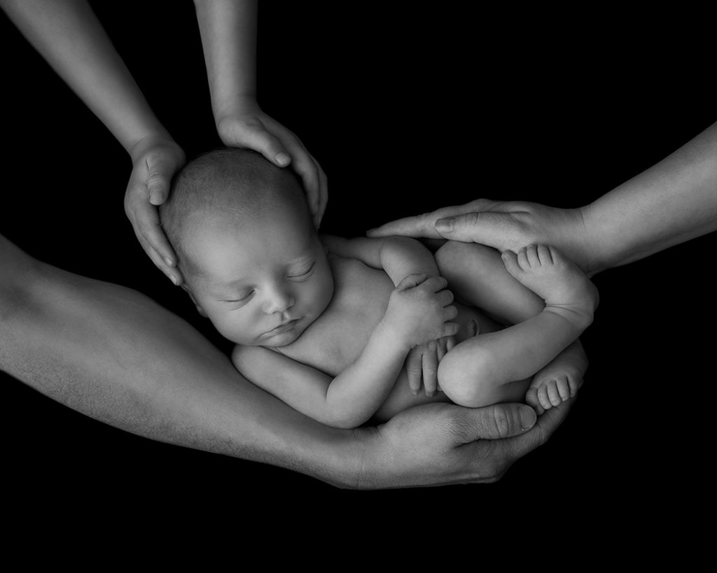 Nyfödd bebis omfamnad av familjens händer