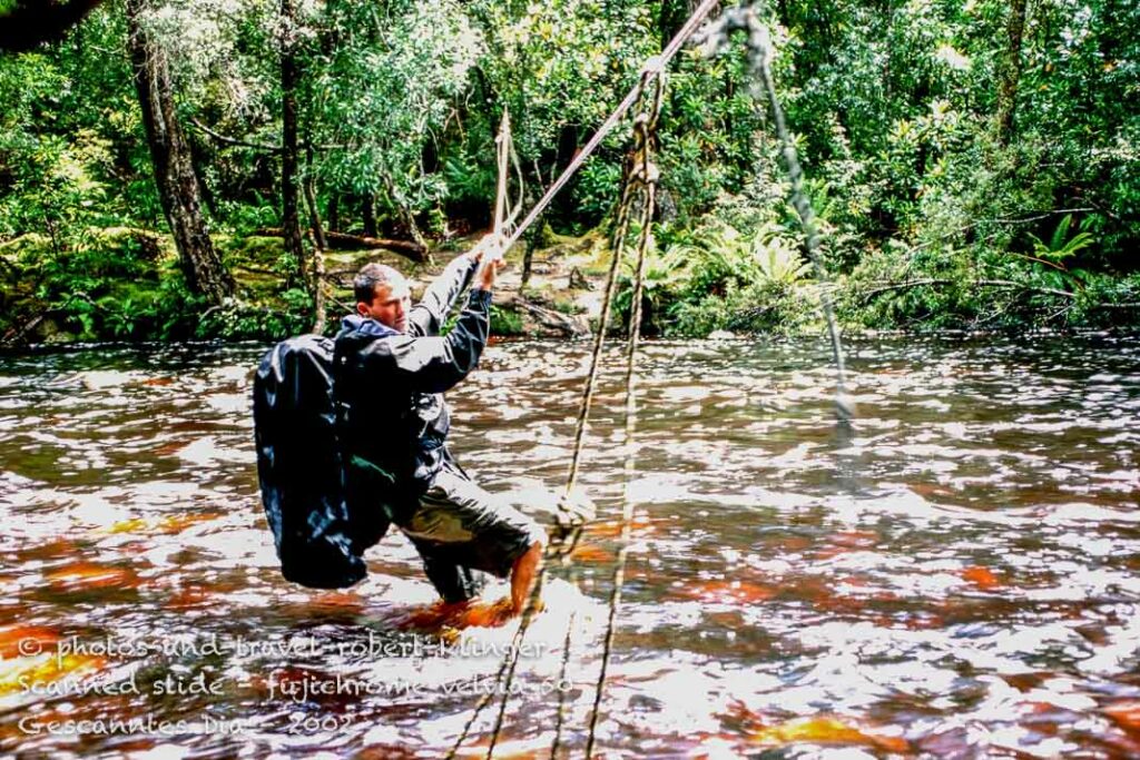 A hiker crossing a river on the Port Davey track with the help of ropes