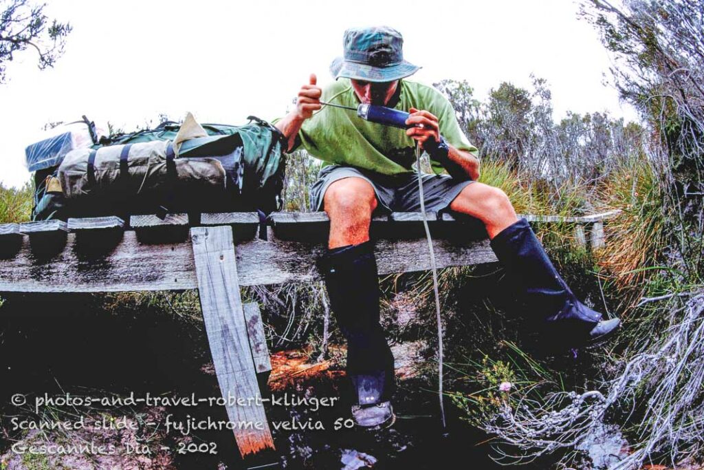 A tramper drinking water out of a stream with a water-filter