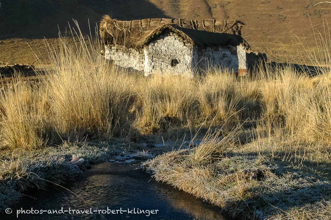 A clay hut hight up in the Andes of Peru with frozen water in front of it