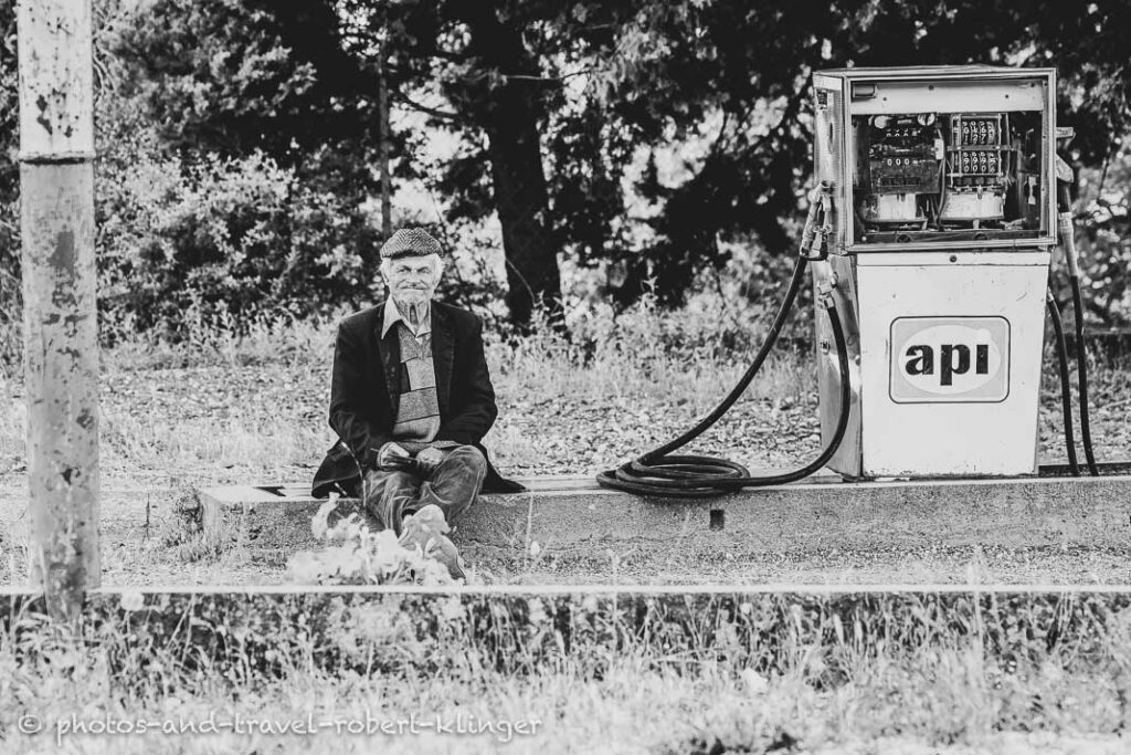 A old man sitting in a fuel station, black and white photo taken in Albania