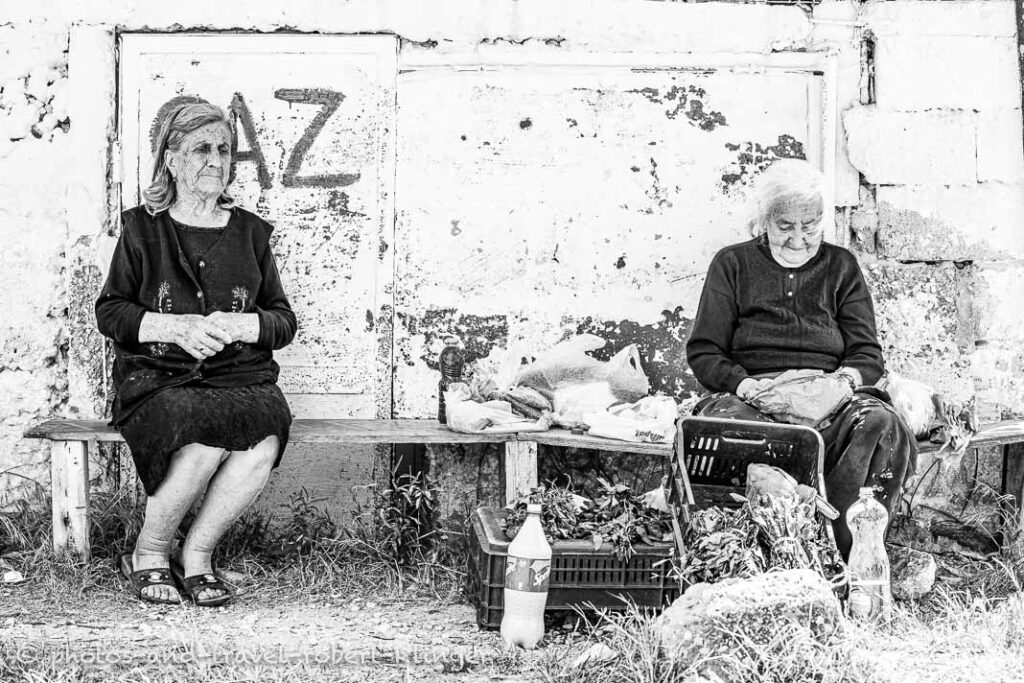 Two old women sitting next to a road and selling vegetables in Albania, black and white photo