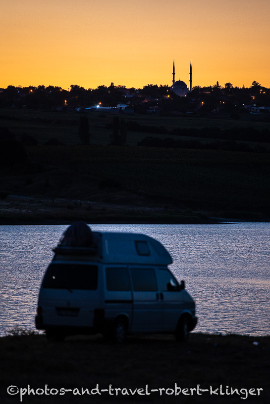 A Volkswagen T4 Syncro Eurovan is parking at a lake in Turkey with a mosque in the background