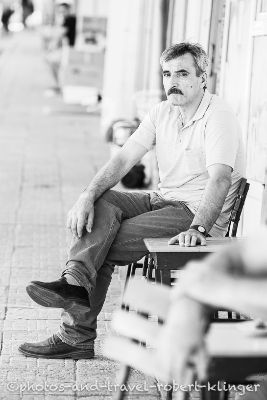 A turkish man sitting in front of a tearoom in Turkey, black and white photo