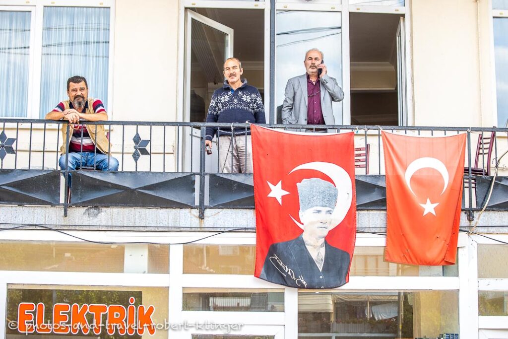 Three men on a balcony in Turkey with a turkish flag and a flag of Atatürk