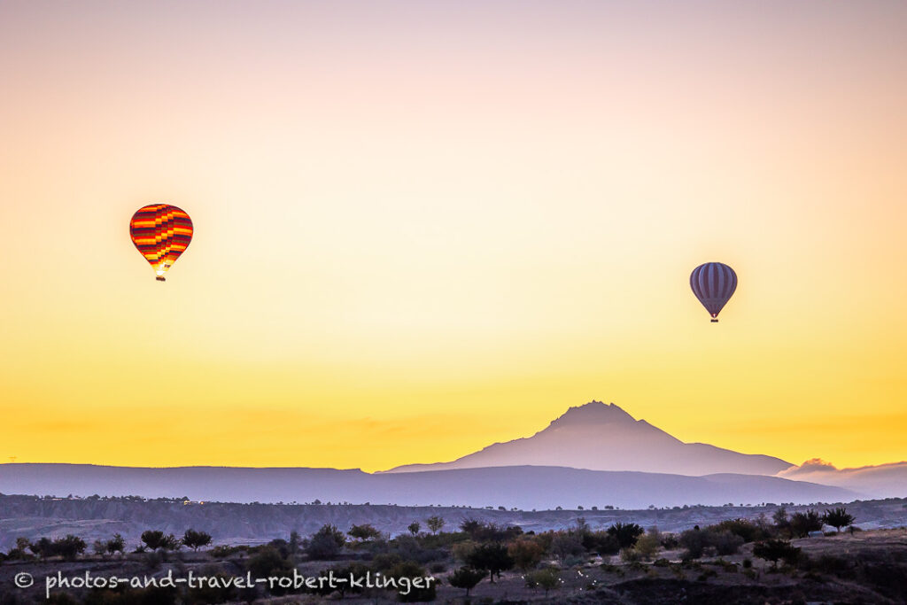 Two hot air ballons flying in Cappadocia before sunrise in front of a volcano