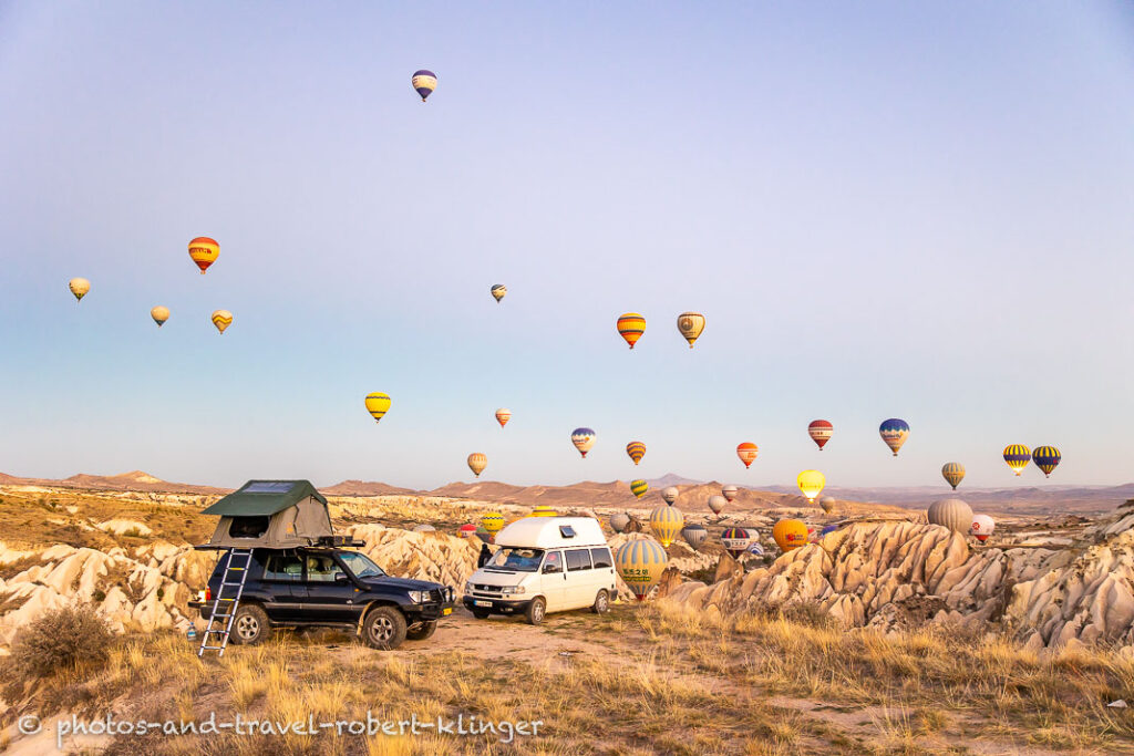 Two camping cars on an early morning in Cappadocia with many hot air ballons in the background