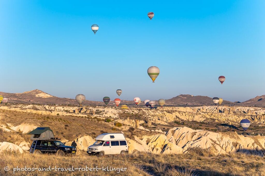 Two camping cars on an early morning in Cappadocia with many hot air ballons in the background