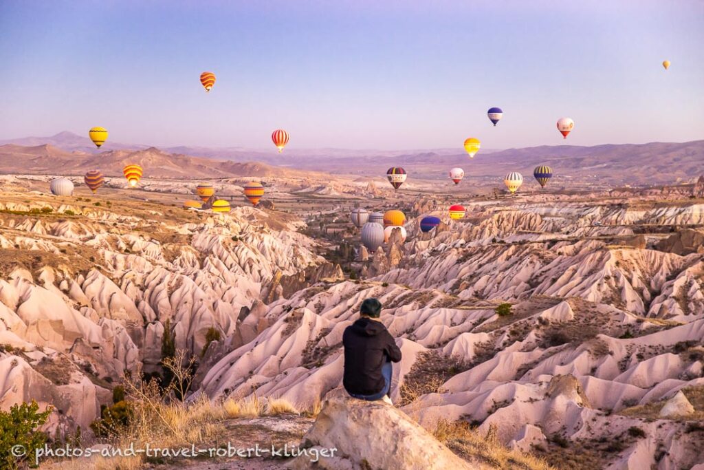 A woman watching many hot air ballons over Cappadocia on an early morning