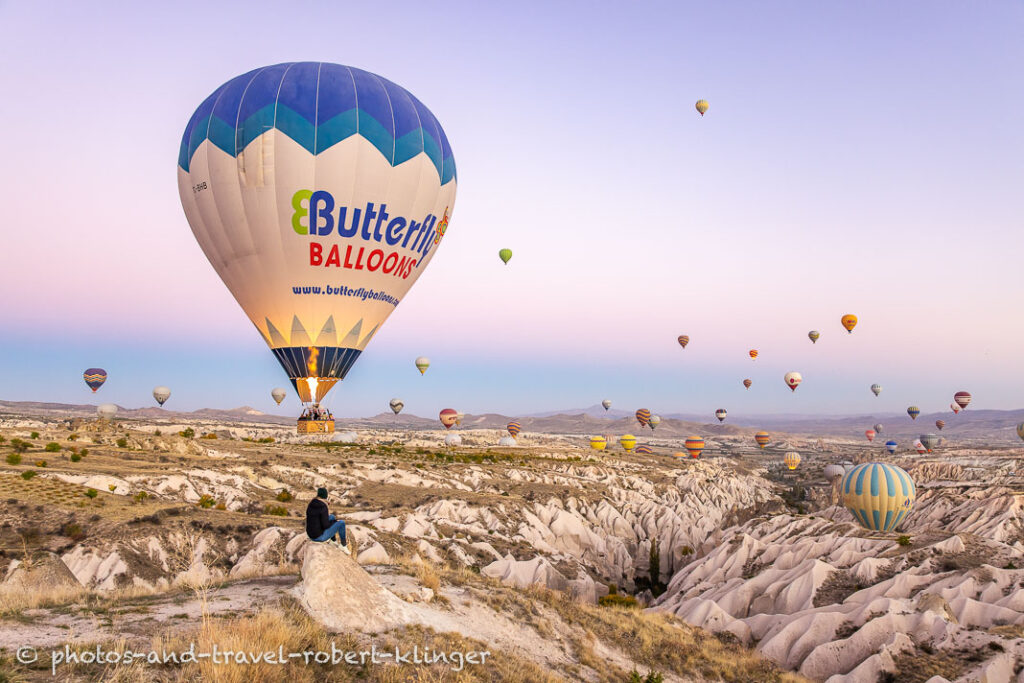 A woman sitting on a rock in Cappadocia and is watching the many hot air ballons on an early morning in Cappadocia